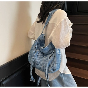 Detailed side view of large blue denim tote bag with vintage belt buckle and frayed edges