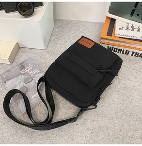Detail of a black canvas crossbody bag with adjustable strap and front zipper compartment