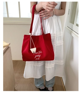 Close-up of red canvas tote bag featuring white embroidered artistic lettering and handles