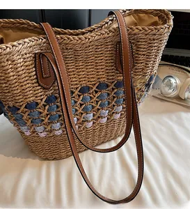 Détail d'un sac cabas en paille tissée avec motifs colorés et anses en cuir marron