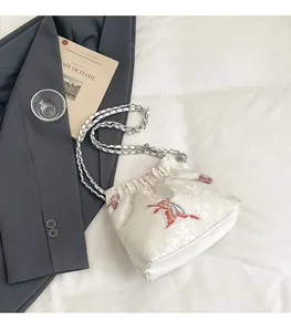 Detail of white jacquard satin bag featuring embroidered butterfly and silver chain strap
