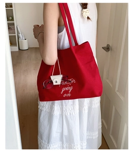 Red canvas tote bag with white lettering on shoulder of a model in a white dress