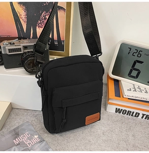 Detail shot of black canvas crossbody bag with brown leather logo patch on grey desk