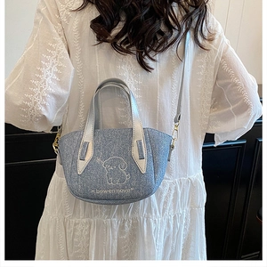 Detail of blue denim shoulder bag with white puppy embroidery and silver leather handle