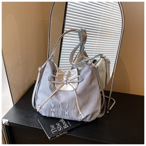Silver-grey tote bag with metallic bow detail and rippled fabric texture on black cabinet