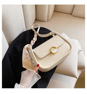 Gros plan d'un sac selle crème avec boucle dorée et foulard en soie sur la poignée