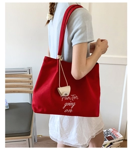 Detail view of a large red canvas tote bag with white lettering and a beige pouch accessory