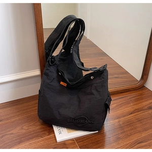 Dettaglio di una grande borsa tote in tela nera con logo ricamato su pavimento
