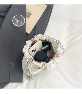 Detail view of cream canvas bucket bag with red floral embroidery and silver chain strap
