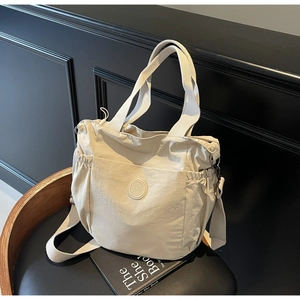 Detail of light beige canvas tote bag with side drawstring pockets and logo badge