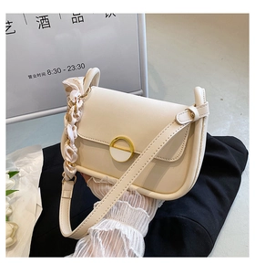 Gros plan d'un sac selle beige avec boucle en métal doré et ruban de soie sur la poignée