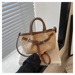 Detailed view of woven straw tote bag with brown leather handles and decorative buckle