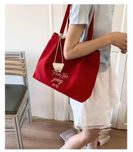 Detail of red canvas tote bag with white script embroidery and small hanging pouch accessory
