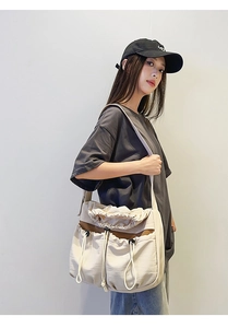 Detailed view of a beige pleated crossbody bag with drawstring pockets and wide strap