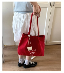 Detail of red canvas tote bag with white script embroidery and decorative rope charm