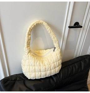 Close-up of pale yellow quilted puff bag featuring a pleated handle and silver zipper