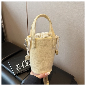 Detail view of yellow bucket bag showing lychee leather texture and drawstring inner bag