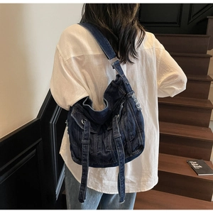 Detail of distressed denim crossbody bag with frayed edges and silver rings on shoulder strap