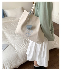Detail of embroidered lettering on cream canvas tote with a light blue leather charm