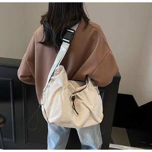Detail of beige drawstring crossbody bag with wide grey strap worn by a model