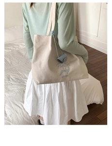 Detail of embroidered blue text on cream canvas tote with a blue leather pendant