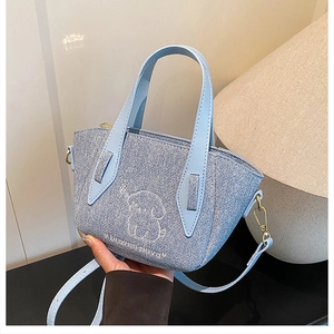 Close-up of light blue denim bag featuring white puppy embroidery and gold hardware