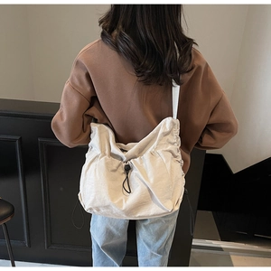 Detailed back view of a beige nylon crossbody bag featuring a black drawstring buckle