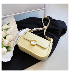 Détail du sac selle jaune clair avec boucle dorée et foulard en soie à fleurs sur fond sombre