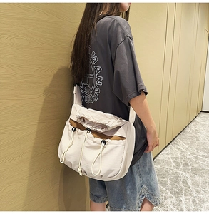 Detail of a large cream crossbody bag with drawstring pockets and wide adjustable strap