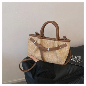 Detail of hand-woven straw tote with brown leather trim and metallic buckle accents