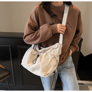 Detail of a large capacity off-white crossbody bag with drawstring design and adjustable strap