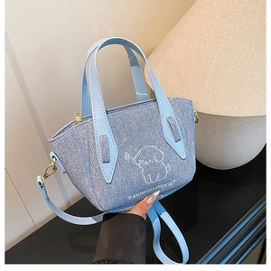 Close-up of a light blue denim bucket bag with white cartoon dog embroidery and handle
