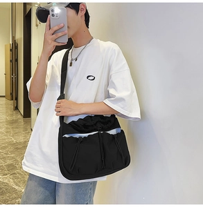 Detail of black pleated crossbody bag with drawstring pockets and white accent trim