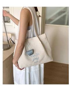 Detail shot of cream canvas tote bag with blue embroidery and earphone case pendant