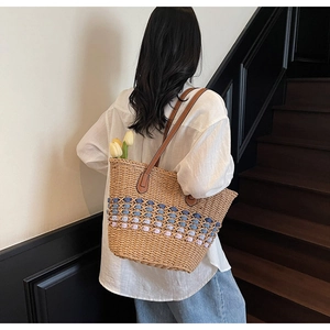 Détail d'un sac cabas en paille tressée avec pompons colorés et anses en cuir brun