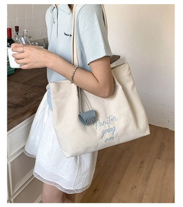 Detailed close-up of beige canvas tote bag featuring blue Pan;Tor embroidered text