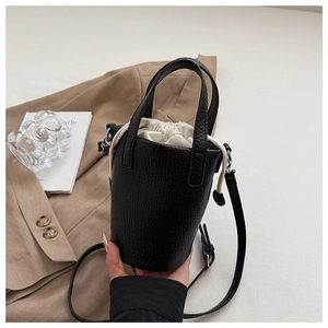 Detail of black leather bucket bag with drawstrings, beige canvas lining and shoulder strap
