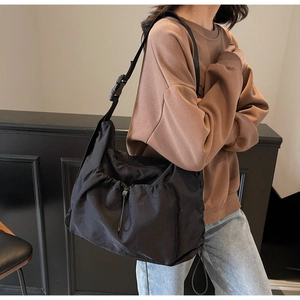 Detail of adjustable strap buckle and drawstring closure on large black nylon crossbody bag