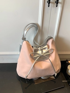 Pink textured tote bag with silver bow accent and metallic handles on a book