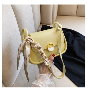 Détail du sac selle jaune clair avec chaîne enroulée d'un foulard et boucle en émail