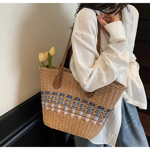 Détail d'un sac cabas en paille tressé avec base colorée et anses en cuir marron