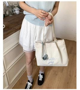 Detail view of cream canvas tote bag with blue 'Pan Tor' embroidery and small blue charm