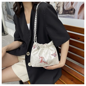 Detail of embroidered butterfly pattern on beige satin drawstring bucket bag with chain strap