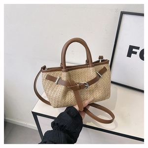 Detail of hand-woven straw crossbody bag with brown leather handles and metal buckle