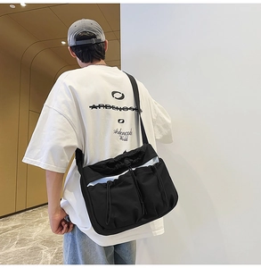Detailed view of black nylon pleated messenger bag with drawstring pockets and wide strap