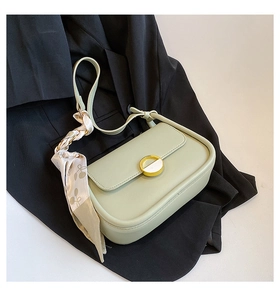 Détail du sac selle vert avec fermoir doré et foulard en soie cerise sur un blazer noir
