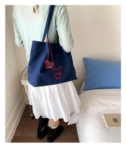Detail of navy canvas tote bag with red embroidery and leather charm shown on shoulder