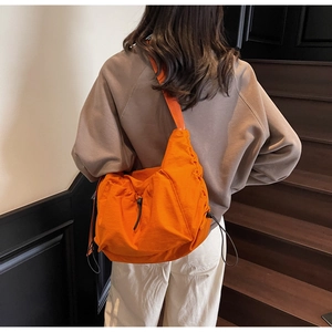 Model wearing a bright orange large canvas crossbody bag with adjustable wide strap