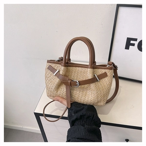 Detail of woven straw handbag featuring brown leather trim, handles and adjustable buckle strap