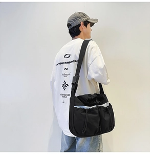 Detail view of black nylon messenger bag featuring drawstring pockets and wide strap